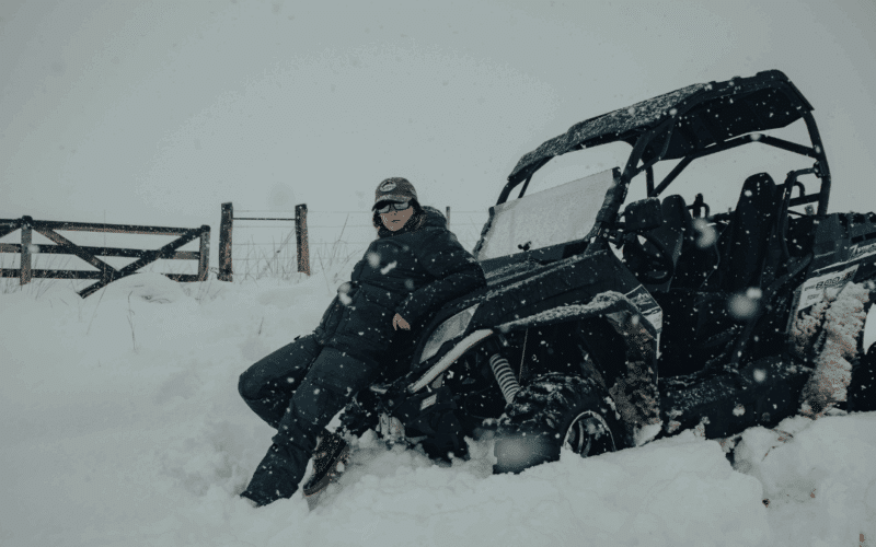 Person in coveralls leaning against a UTV in the snow