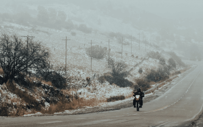 Person riding motorcycle in winte rwith snow on ground next to road
