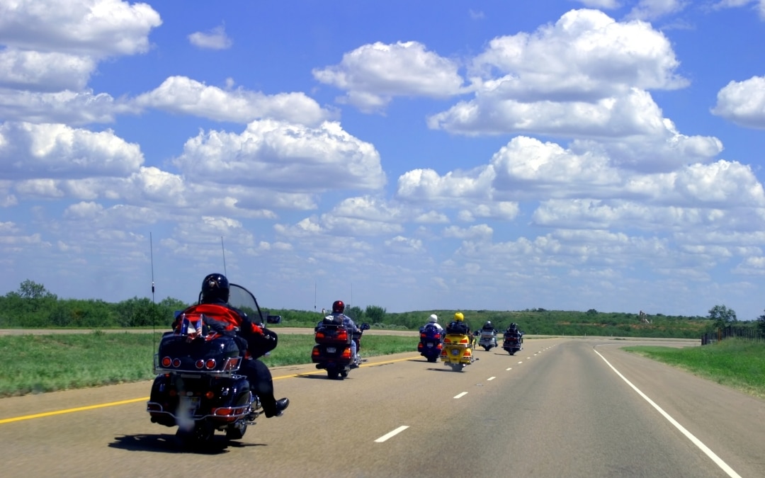 Motorcycle riders on a highway with a partly sunny sky and clouds