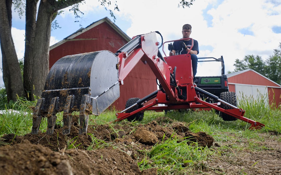 DirtMaster towable backhoe digging a trench on a rural property